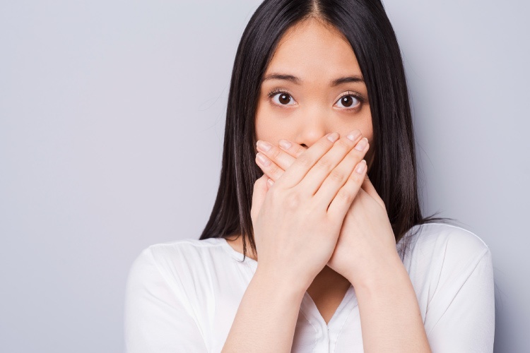 Brunette woman coves her mouth with her hands due to swollen gums