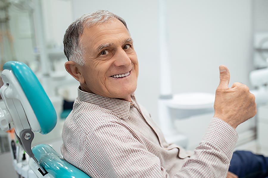 Gray haired man gives the thumbs up sign from the dental chair.