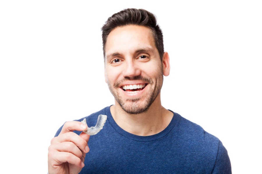 Smiling man holding a clear aligner.