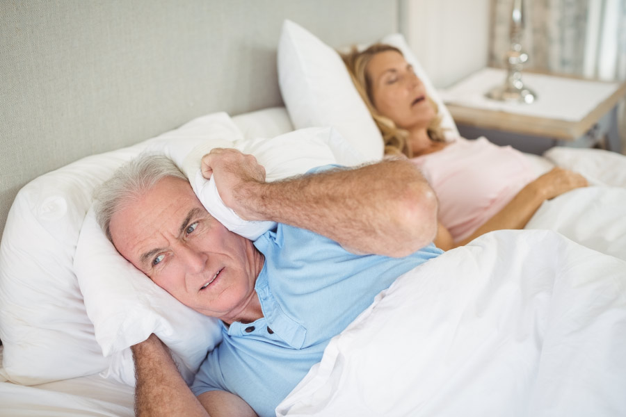 Man covering his head with his pillow to block his wife's snoring.