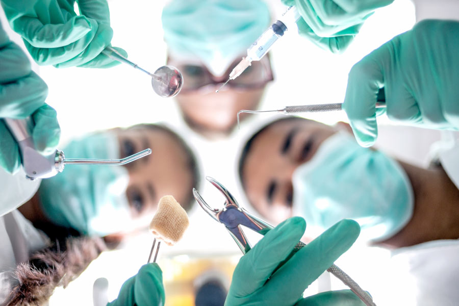 Masked dental professionals ready to perform oral surgery are looking down on the patient.