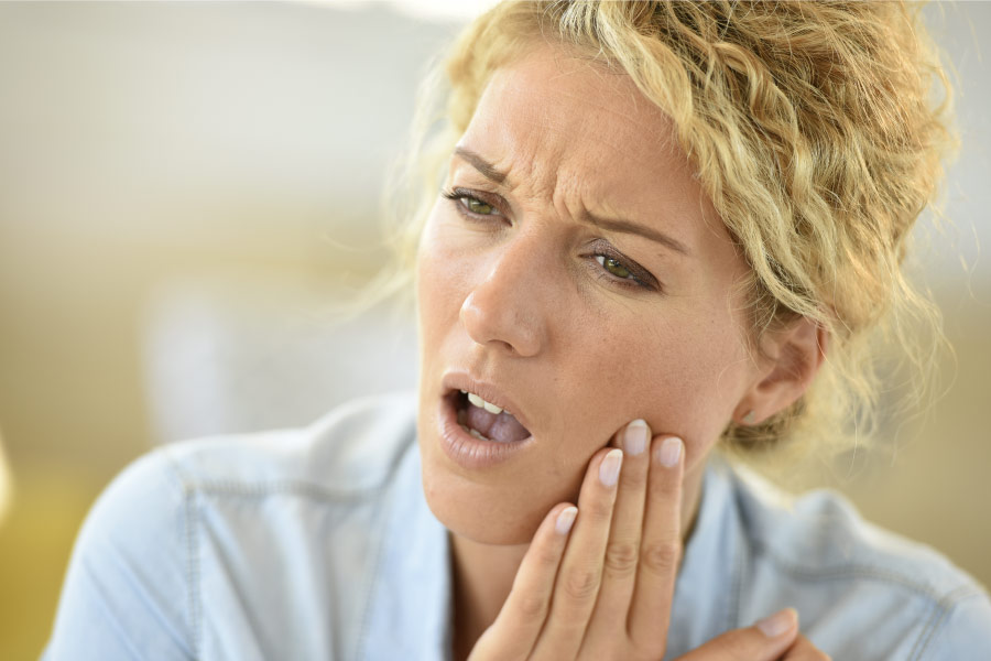 Blonde woman with her hand to her cheek due to a toothache.